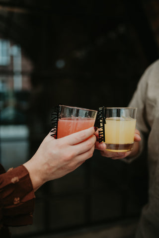 Two people holding glasses of drinks against a dark background