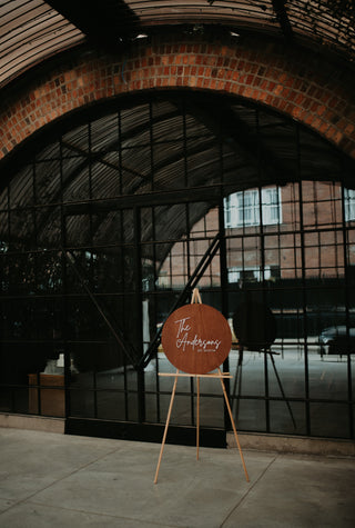 Wooden sign on a stand in front of a large arched window with brick archway.