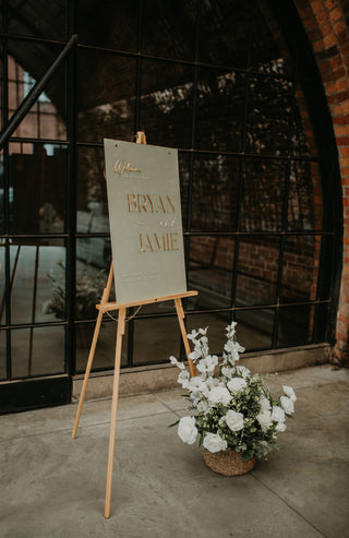 Easel with a wedding sign and flowers in front of a brick wall.