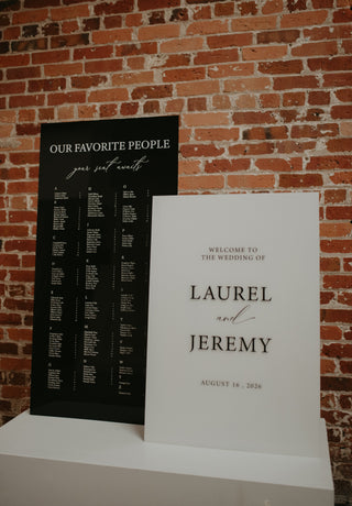 Two wedding signs against a brick wall, one black and one white, with text about favorite people and wedding details.